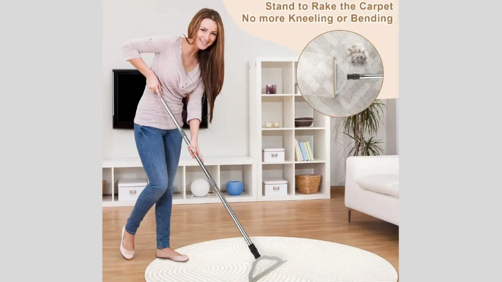 “Close-up of a long handle carpet rake lifting pet hair and dirt from carpet.”